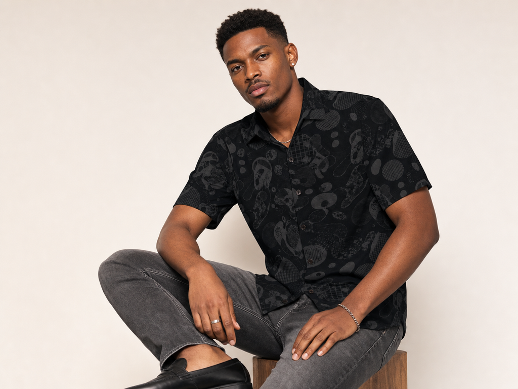 Male model wearing the Rich and Rich Men’s Black Fusion Designer Shirt with a boxy fit, short sleeves, notch lapel collar, and bold black fusion designer pattern.