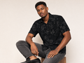 Male model wearing the Rich and Rich Men’s Black Fusion Designer Shirt with a boxy fit, short sleeves, notch lapel collar, and bold black fusion designer pattern.