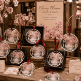Round crystal glass ornament with pink cherry blossom tree artwork and coordinating hanging ribbon