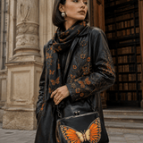 Orange waxed PU leather kisslock crossbody bag with monarch artwork and rivet-accented straps